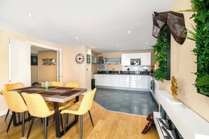Eine moderne Küche mit weißen Schränken, einer zentralen Kochinsel und einem Essbereich mit Holztisch und gelben Stühlen.
