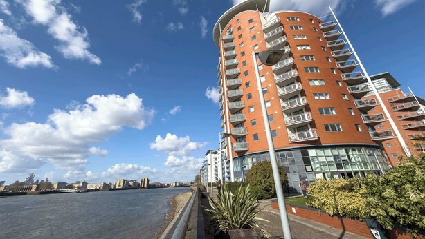 A multi-story residential building with balconies, a clear sky, and a river in the background. - Stunning Thames View 2BR Apartment 2 Baths 2 Balconies Sleeps 6 (Greater London)