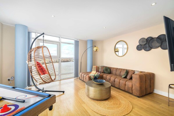 Uma sala de estar moderna com uma janela grande, uma cadeira suspensa, um sofá e uma mesa de centro.