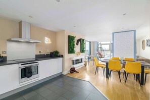 A modern kitchen with a dining area, featuring a coffee machine, a foosball table, and a view of the city. - Stunning Thames View 2BR Apartment 2 Baths 2 Balconies Sleeps 6 (Greater London)