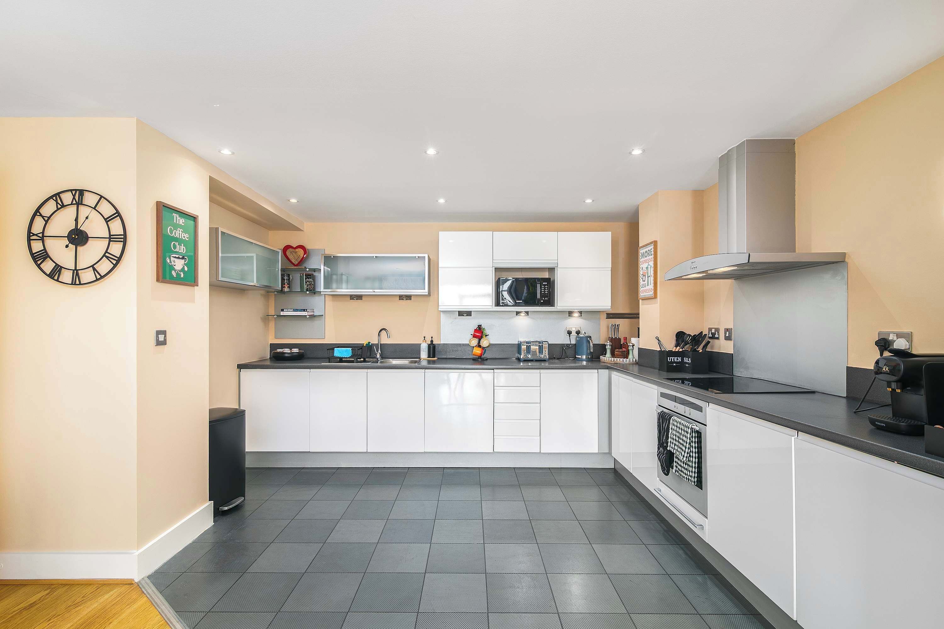 A modern kitchen with white cabinets, a black countertop, a built-in microwave, and a coffee machine.
