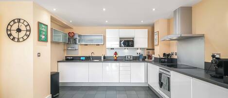 A modern kitchen with white cabinets, a black countertop, a built-in microwave, and a coffee machine.