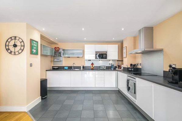 A modern kitchen with white cabinets, a black countertop, a built-in microwave, and a coffee machine.