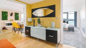 A modern living room with a yellow accent wall, a large mirror, and a dining area with yellow chairs.