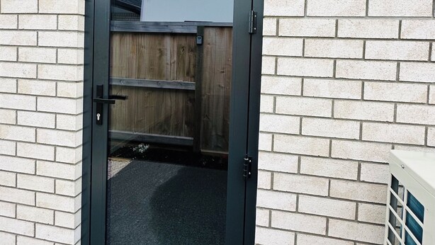 Una puerta enmarcada en negro con un panel de vidrio, ubicada en una pared de ladrillo.