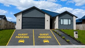 Un edificio moderno con dos espacios de estacionamiento para huéspedes señalados con líneas amarillas y el texto 'GUEST PARKING'.