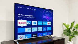 Un televisor de pantalla plana montado en un mueble de entretenimiento de madera oscura, con una planta en maceta a su lado.