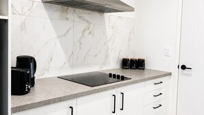 Una cocina moderna con campana de acero inoxidable, armarios blancos, salpicadero de mármol y cocina de inducción negra.