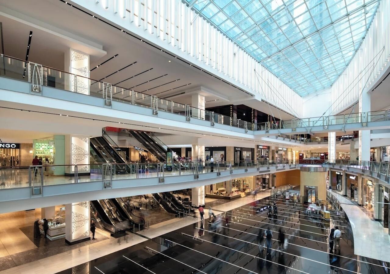 Un centre commercial à plusieurs niveaux, doté d’escaliers mécaniques reliant les étages, de toits en verre et de divers magasins de vente au détail.