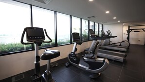 A gym with cardio machines, a rowing machine, and a view of a body of water through large windows.