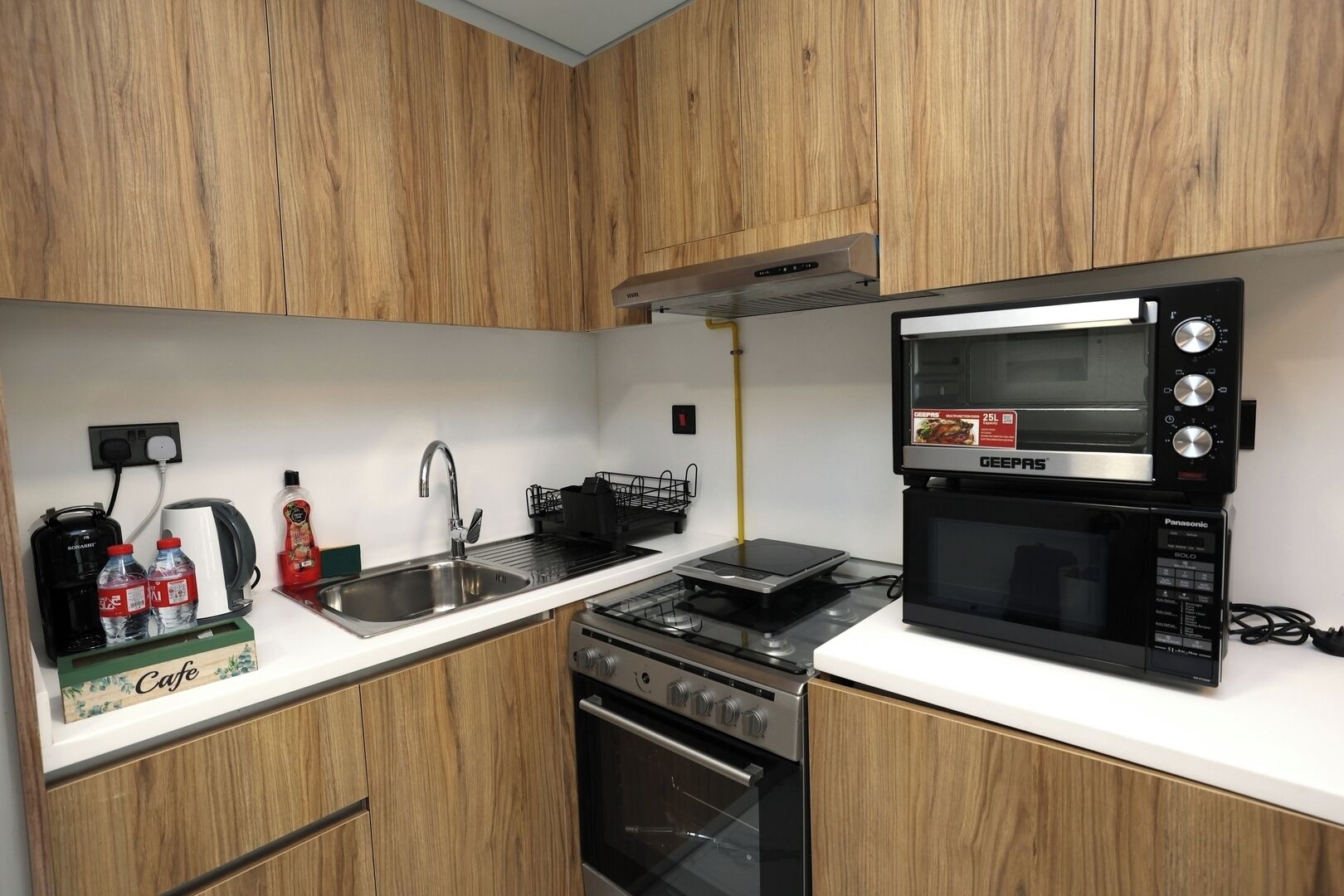 Une cuisine compacte équipée d’un four à micro-ondes GEPEAS, d’une cuisinière et d’un évier.