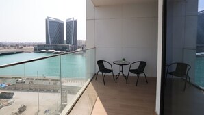 A balcony with a view of a marina and two modern buildings. There are two chairs and a small table.