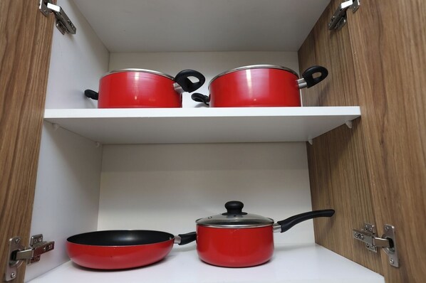 A kitchen with a white countertop, a red frying pan, and two red pots on a white shelf.