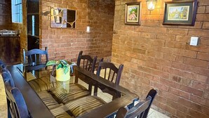 A dining area with a brick wall, framed pictures, and a table with chairs.