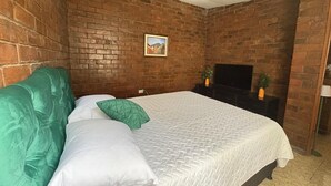 A bedroom with a brick wall, a bed with green and white bedding, a TV on a stand, and a small picture on the wall.