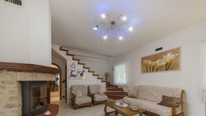 Una sala de estar con chimenea, una escalera, sofás estampados y un lámpara en el techo.