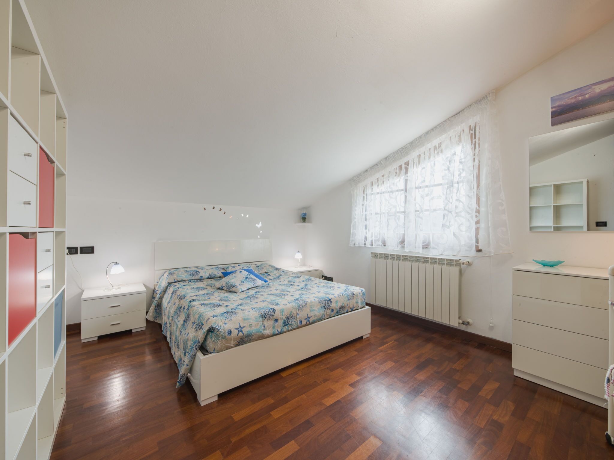 Een slaapkamer met een bed, nachtkastje, dressoir, raam met gordijnen en een radiator.