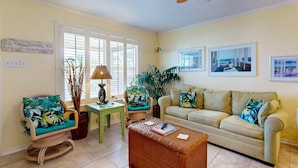 A living room with a beige sofa, a wicker coffee table, a wicker chair, a small side table, and a potted plant. - Shared Pool, Pet Friendly, Garage Access (Port Aransas)