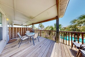 A wooden deck with a table and chairs, overlooking a swimming pool and palm trees. - Shared Pool, Pet Friendly, Garage Access (Port Aransas)