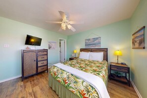 A bedroom with a bed, a television, a ceiling fan, a nightstand with a lamp, and a door. - Shared Pool, Pet Friendly, Garage Access (Port Aransas)