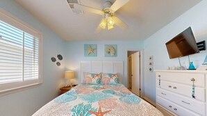 A bedroom with a bed, a ceiling fan, a dresser, a TV, and wall decorations. - Shared Pool, Pet Friendly, Garage Access (Port Aransas)