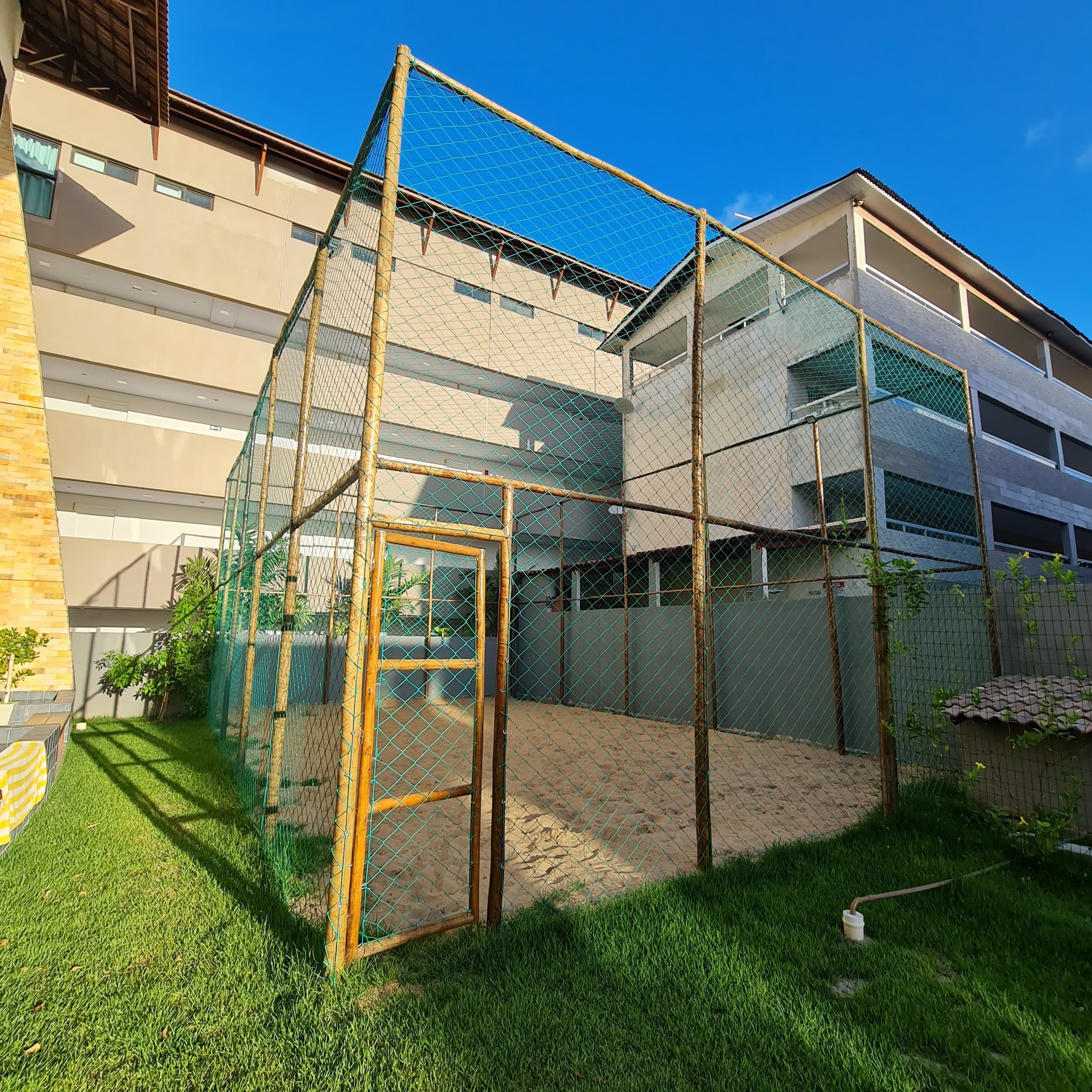 A fenced outdoor area with artificial grass, a wooden structure, and a building in the background.