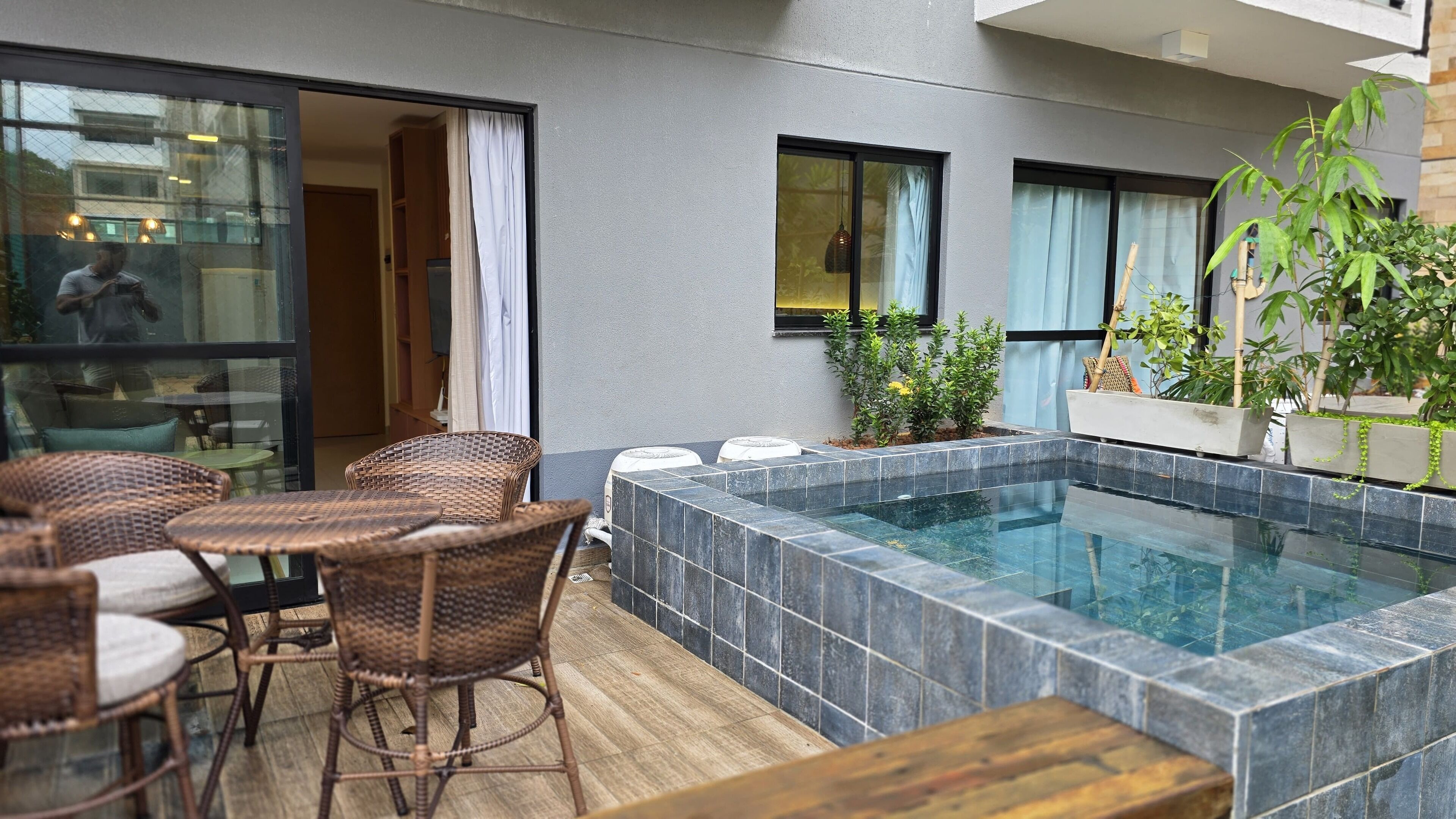A modern outdoor pool area with a hot tub, wicker furniture, and potted plants.