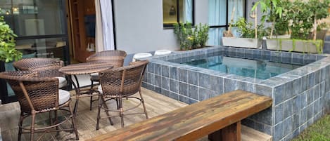 A modern outdoor patio with a hot tub, wicker furniture, and a wooden bench.