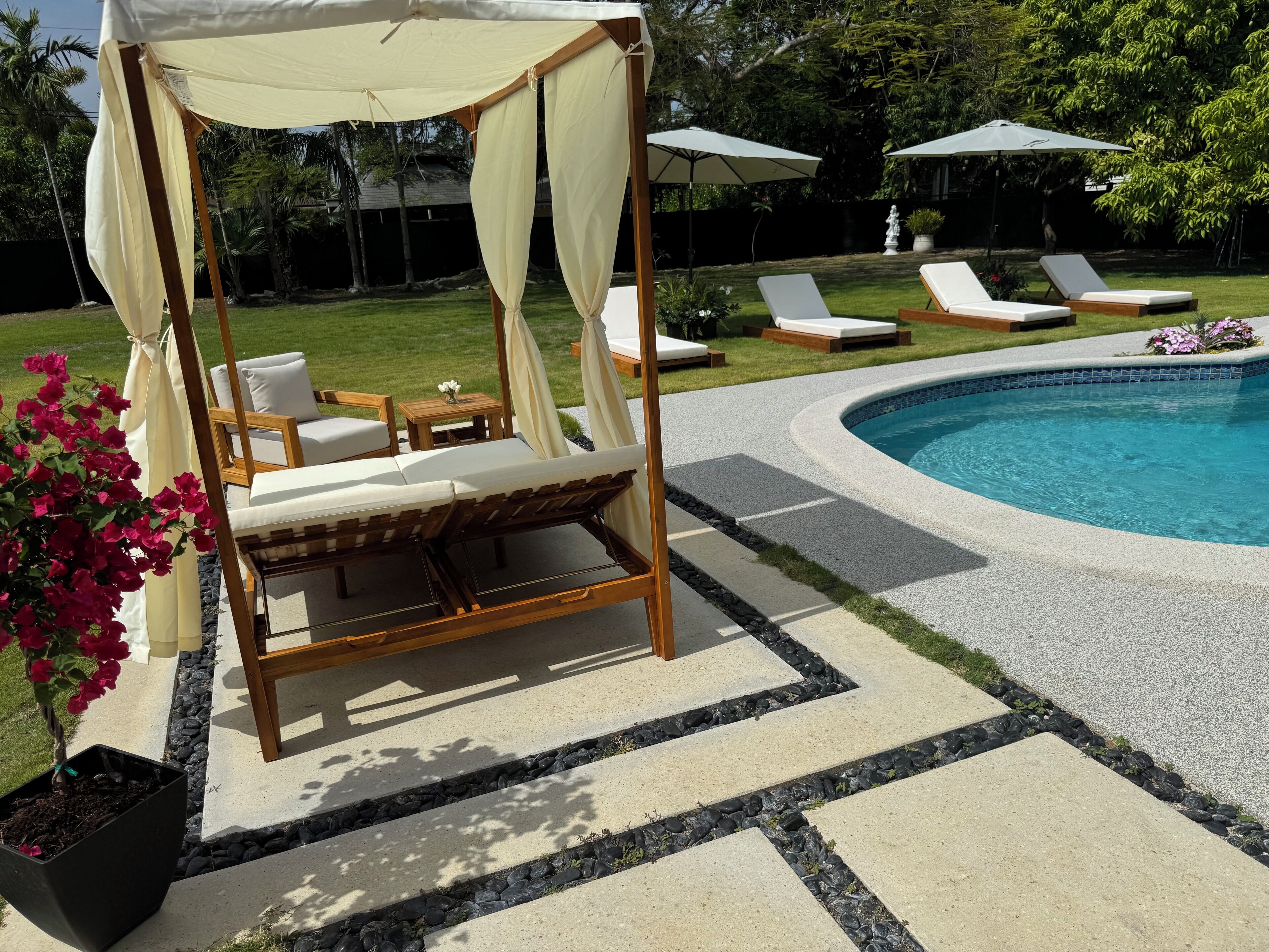 A poolside area with a wooden canopy bed, lounge chairs, and a swimming pool.