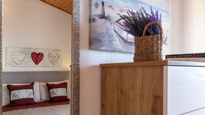 A bedroom with a wooden cabinet, a bed with red and white pillows, a wall with heart-shaped decorations, and a painting of a boat. - Casa Tonina by Interhome (Pittulongu)