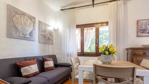 A cozy living room with a grey sofa, a wooden dining table, and a vase of yellow flowers. - Casa Tonina by Interhome (Pittulongu)