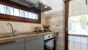 A kitchen with a sink, stove, oven, and window with blinds. - Casa Tonina by Interhome (Pittulongu)