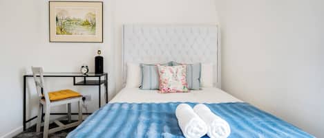 A neatly arranged bedroom with a bed, a desk, and a chair.
