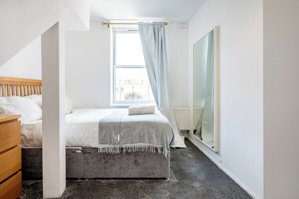Un dormitorio con cama, cómoda, ventana con cortinas y radiador.