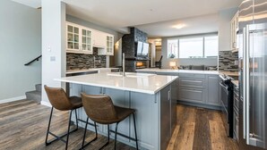 A modern kitchen with a large island, bar stools, and a built-in TV. - 2 Side-by-Side Ski-In/Ski-Out Townhomes | Sleeps 19 w/ Views (Silver Star Mountain)