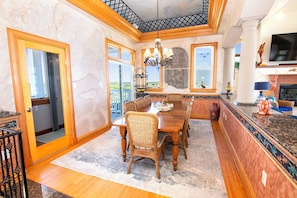A dining area with a wooden table, wicker chairs, a chandelier, and a view through large windows.