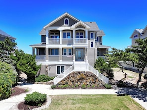A multi-story residential building with a stone foundation, a balcony on the second floor, and a driveway leading to the entrance.