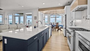 A modern kitchen with a large island, built-in appliances, and a view to the outside. - A Wave From It All | Oceanfront | Hot Tub (Virginia Beach)