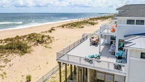 A beachfront property with a deck overlooking the ocean, featuring outdoor seating and a view of the beach. - A Wave From It All | Oceanfront | Hot Tub (Virginia Beach)
