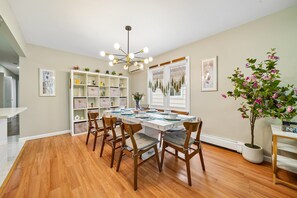 A dining area with a wooden table, chairs, a chandelier, a bookshelf, and a potted plant. - Spacious Modern 3BR Free Parking 30 min to NYC (Jersey City)