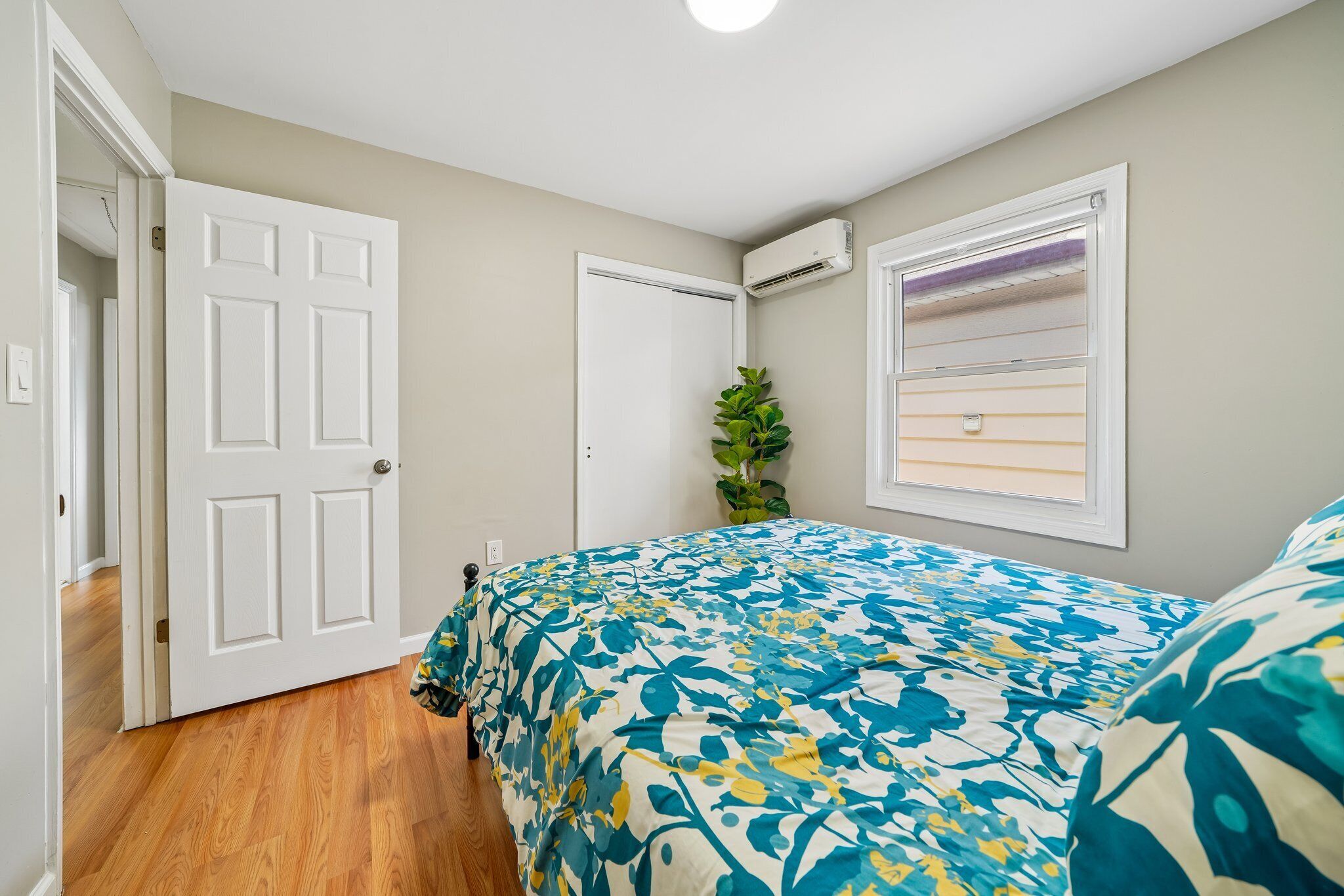 A bedroom with a bed, a potted plant, and a window with blinds.