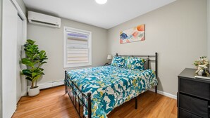 A bedroom with a bed, a potted plant, a window with blinds, an air conditioning unit, and a wall-mounted artwork. - Spacious Modern 3BR Free Parking 30 min to NYC (Jersey City)