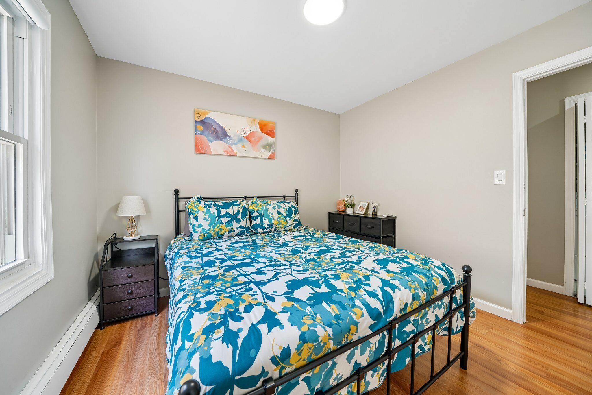 A bedroom with a bed, bedside table, nightstand, and a wall-mounted painting.