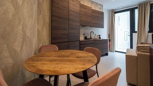 A modern living room with a round wooden table and matching chairs, a sofa, and a kitchen area with dark wood cabinets and a sink. - VLC HOST - Palleter 1 (Valencia)