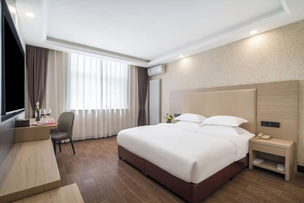 A hotel room with a large bed, a desk, a chair, a TV, and a window with curtains.