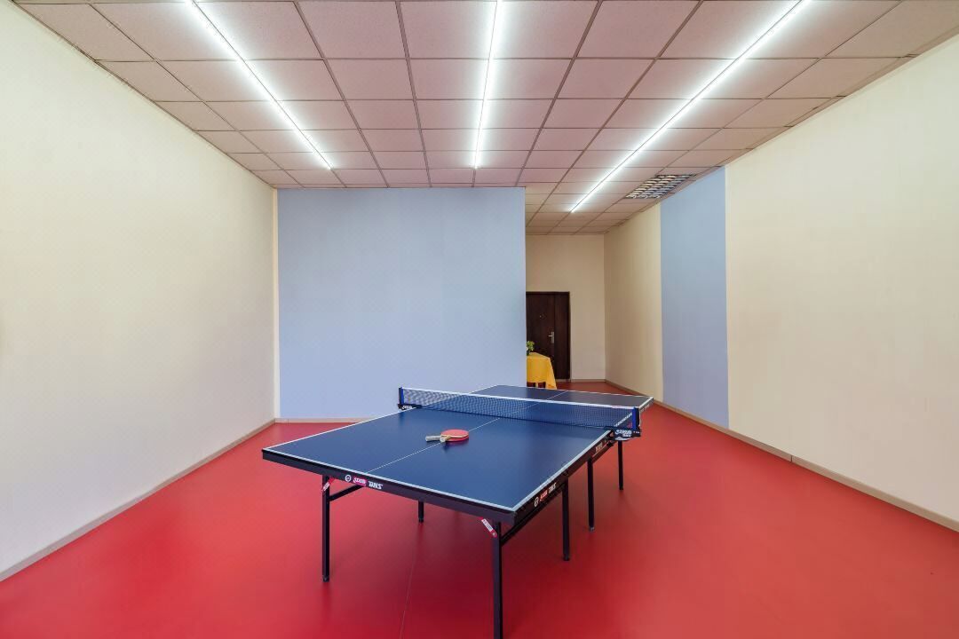 A ping pong table in a room with red flooring and white walls.