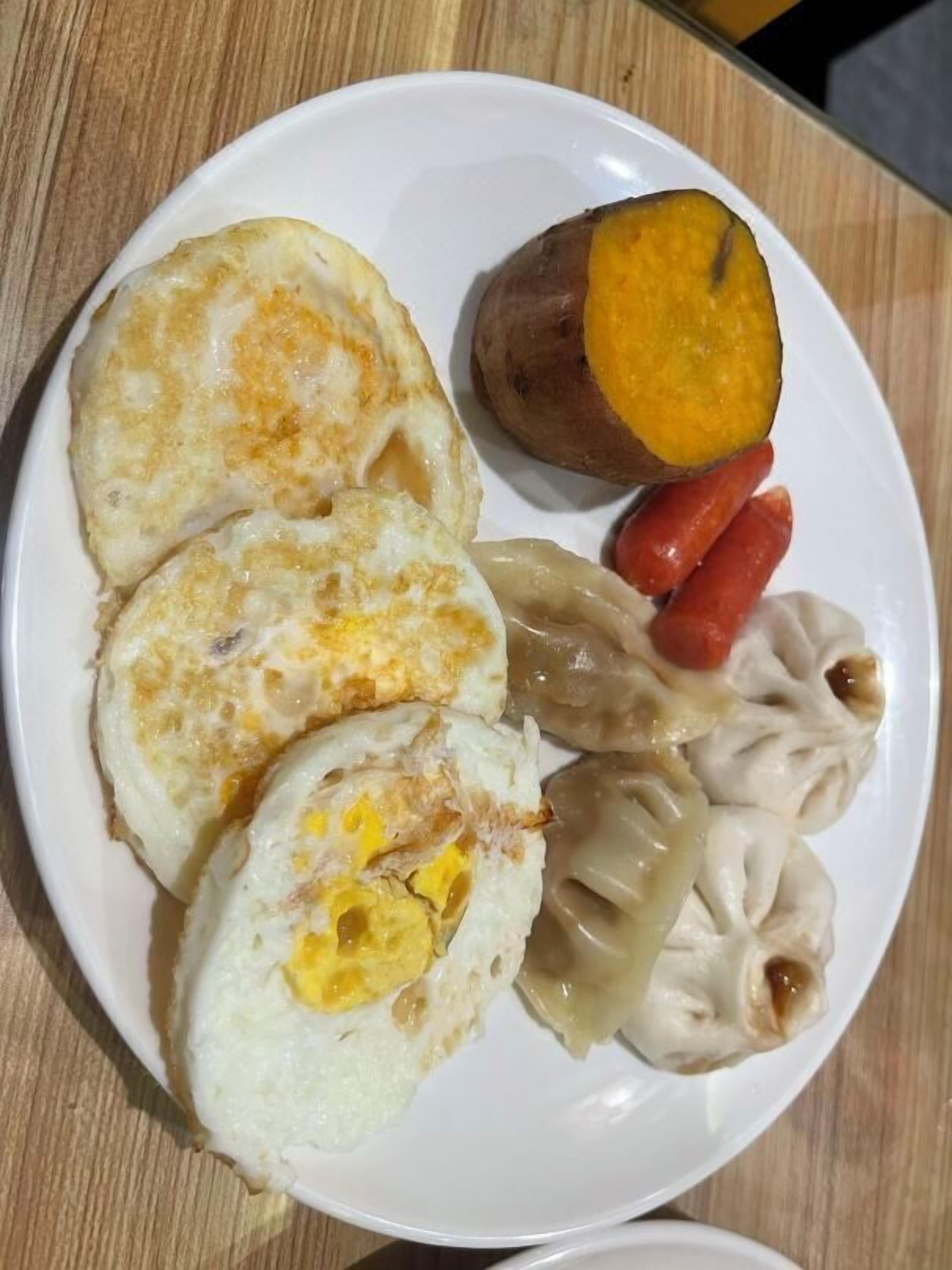 A plate with three fried eggs, a half-cut sweet potato, and dumplings.