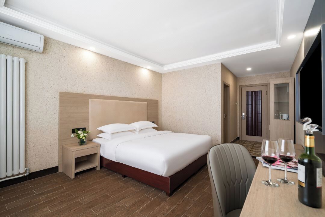 Habitación de hotel con cama, mesita de noche, una silla, escritorio con botella y vasos, y televisor.