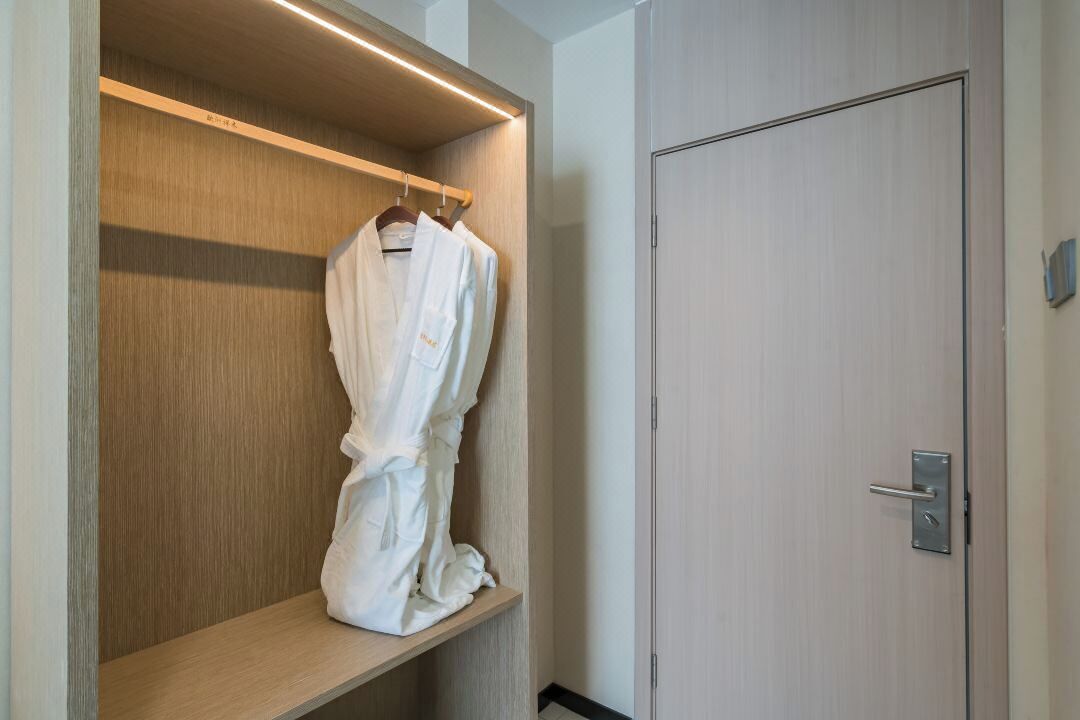 A walk-in closet with a wooden shelf and a hanging robe.