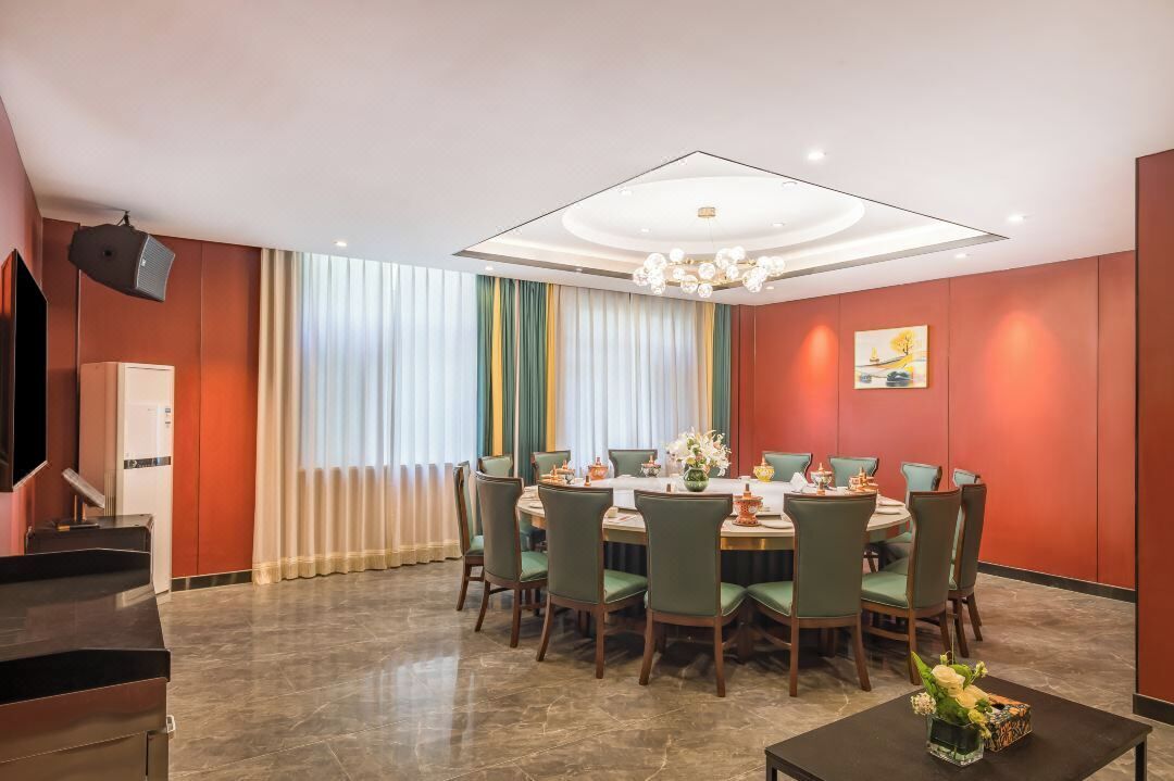 Un coin repas avec une table ronde, des chaises vertes et un lustre.